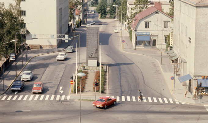 Kesäinen katunäkymä Kymen Lukolta v. 1970.  Kuvassa Vapauden patsas  Salpausselänkadun ja Kauppalankadun risteyksessä. Kuvassa henkilöautoja ja Salpaussselänkadun rakennuksia.