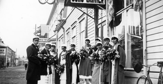 Kouvolan Suomalaisen Yhteiskoulun ylioppilaat Juho Mannerin kahvilan edustalla Kauppalankadulla keväällä 1924. Kirjoitukset läpäisi 8 tyttöä ja 3 poikaa. Yksi poika puuttuu kuvasta.