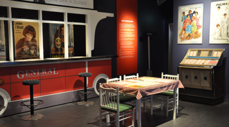 Ravintola Red Car Kouvolan kaupunginmuseon Mannerin lipan alla –näyttelyssä. Pöytä ja neljä tuolia baaritiskin edessä.
