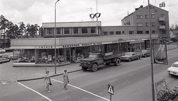 Torinlyhdyn liikerakennus Päätekadun ja Valtakadun (nykyinen Kouvolankatu) kulmauksessa toukokuussa 1969. Rakennuksessa toimi Valtakadun puolella Corsette, Kouvolan Paperi ja Lelu, Silmäoptiikka, Hokkasen Asuvalinta sekä Juho Mannerin kahvila. Kuvaaja Eero Suikki.