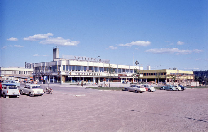 Kuusankosken keskustaa kesällä 1969. Etualalla on vuonna 1965 valmistunut Yhdystalo ja oikealle on valmistumassa Ostoskeskuksen liikerakennus. Kuvaaja tuntematon.