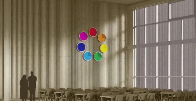 Seinällä digitaalinen, pyöreä väriympyrä, jossa seitsemän eri väriä: punainen, oranssi, keltainen, vihreä, vaaleansininen, sininen ja violetti. Vasemmalla kaksi ihmistä katselee selin seinällä olevaa väriympyrää. Etualalla pöytiä tuoleineen.