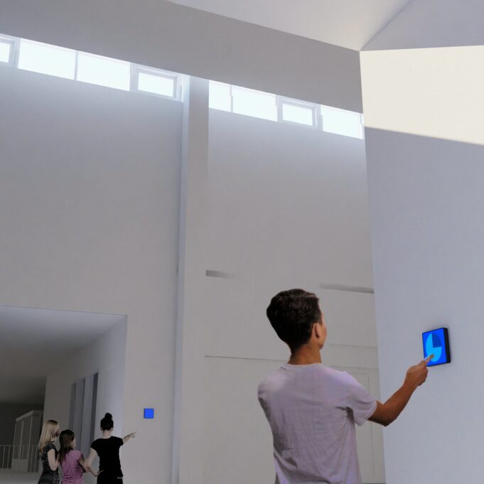 Etualalla selin oleva poika koskettamassa sormella seinällä olevaa neliönmuotoista sinisen väristä pientä digitaalista näyttöä. Takana selin kolme tyttöä, joista oikealla oleva osoittaa kädellä seinällä olevaan neliön muotoiseen sinisen väriseen digitaaliseen näyttöön.