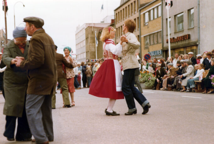 Kansallispukuun pukeutunut nainen tanssii miehen kanssa Kouvolan kadulla, jossa myös muita tanssimassa.