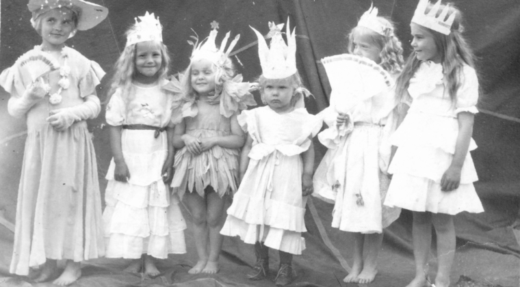 6 pientä tyttöä vaaleisiin mekkoihin pukeutuneina, päässä itse tehdyt kruunut.