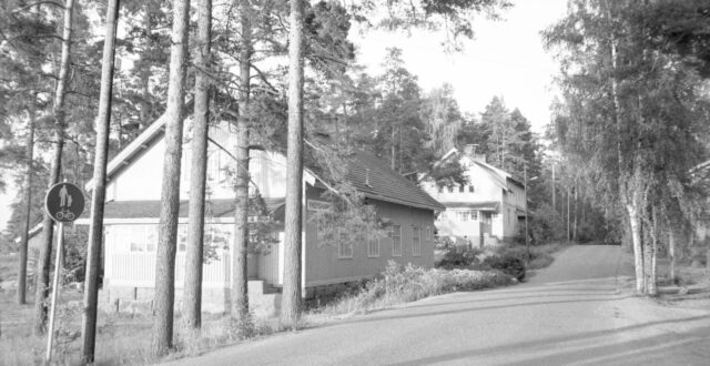 Mustavalkoinen kuva kadusta jonka varrella on puutaloja.