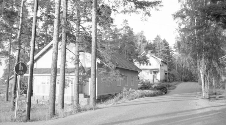 Mustavalkoinen kuva kadusta jonka varrella on puutaloja.
