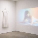 Seinälle heijastettu videoprojisointi ja seinällä henkarissa valkoinen mekko.